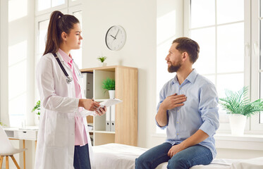Young man sitting on the couch in the doctor's office and pointing to his chest to the doctor...