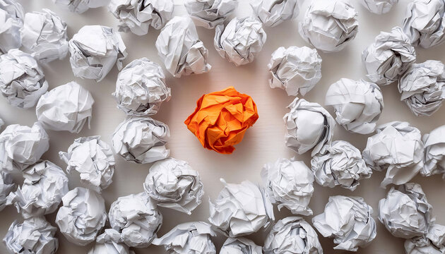 Crumpled white paper balls spread out with one orange ball in the center, symbolizing standing out and uniqueness among many. Flat lay.