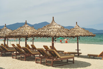 Straw sunshades and sunbeds on the empty pebble beach with sea in the background. Deserted beach with rattan sun loungers and umbrellas
