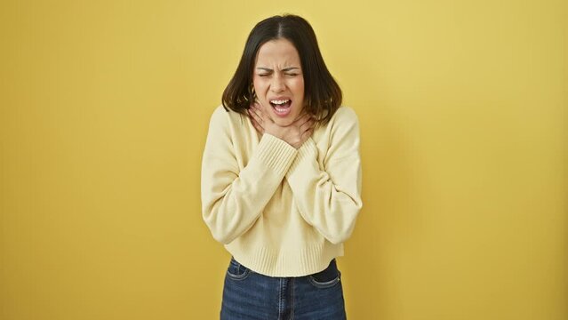 Young hispanic woman in pain, choking in her beautiful yellow sweater, isolate on background. health problem - violent asphyxiate, suffocate or strangle assault.