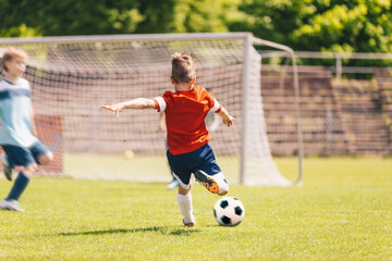 Obraz premium Little Boy Kick Soccer Ball During League Match. Happy Kid Have Fun Shooting Ball Towards Soccer Goal. School Soccer Tournament Game For Kids