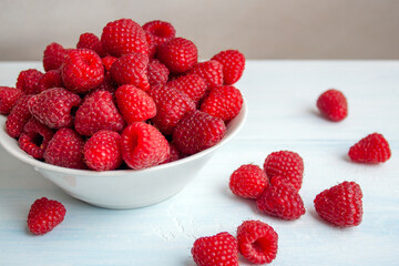 fresh raspberries in a white bowl on a light blue table background