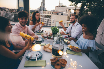 Group of friends having fun on the rooftop of a beautiful rooftop. Young people celebrating on a modern terrace with the view at the aperitif time. 