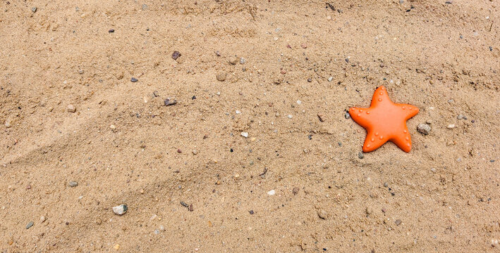 Orange toy starfish on golden sand.
