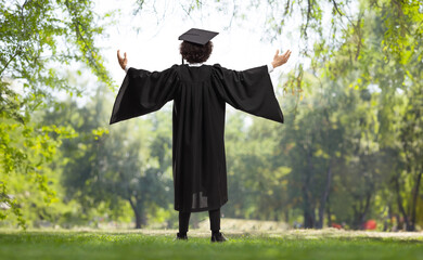 Rear view shot of a happy male student in a graduation gown in a park