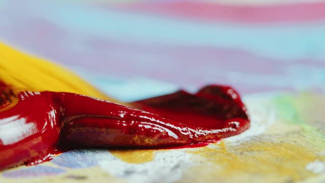 Dipping paintbrush in red oil paint squeezed on paper or palette. Extreme close-up shot