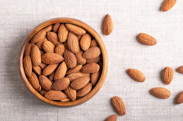 Almonds in a wooden bowl on linen fabric. Shelled, raw, whole and dried nuts, botanically drupes, seeds and fruits of Prunus dulcis. Ready-to-eat as a snack, or used as an ingredient for baking. Photo
