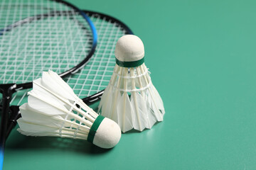 Feather badminton shuttlecocks and rackets on green background, closeup. Space for text