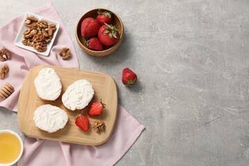 Delicious bruschettas with ricotta cheese, strawberries, walnuts and honey on grey textured table, flat lay. Space for text