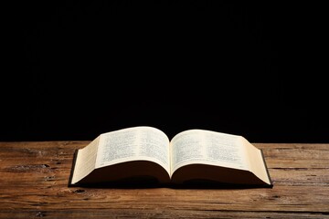 Bible on wooden table against black background, space for text. Religion of Christianity