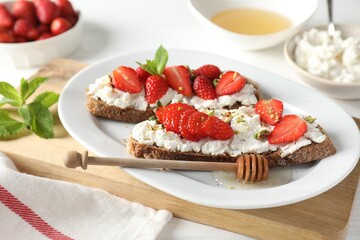 Delicious ricotta bruschettas with strawberry, mint, pistachios served with honey on white table