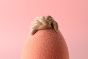 Makeup sponge with skin foundation on pink background, closeup