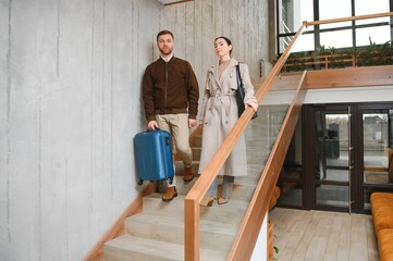 Fototapeta premium Happy couple entering the hotel pulling their luggage, vacation concept