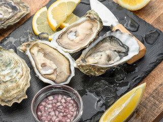 Opened raw oysters with sauce and lemon slices on gray stone serving board. Delicacy food. © volff