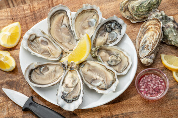 Opened raw oysters with sauce and lemon slices on plate on wooden table. Top view. © volff