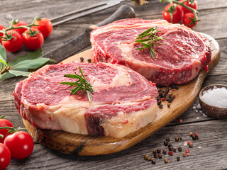 Raw beef steaks with herbs and spices ready for cooking are on wooden board.