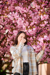 Woman allergic suffering from seasonal allergy at spring in blossoming garden at springtime. Young...