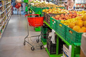 plastic basket with products near a display case with vegetables and fruits in a supermarket