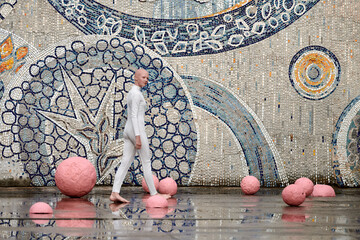 Young hairless girl ballerina with alopecia in white futuristic suit dancing outdoor among pink...