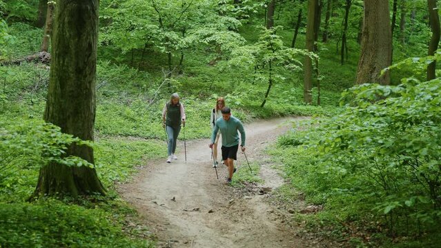 Trainer show how walking use Scandinavian trekking sticks and hold nordic poles in green forest. Man and women