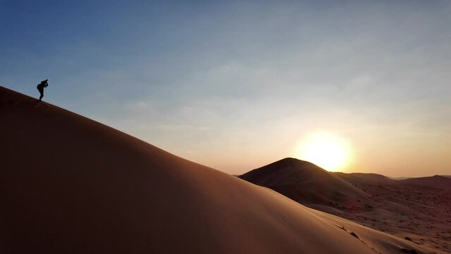 Woman photographer on the dunes of Empty Quarter Rub' al-Khali desert of Oman at sunset.