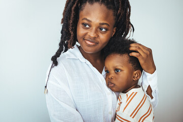 A young black boy finds solace in his mother's embrace while at a doctor's office, both dressed casually, reflecting a nurturing moment in a clinical setting.