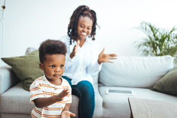 Fototapeta premium A smiling African American mother engages with her son in their cozy living room, displaying a casual yet lovely family moment in a nurturing domestic setting.