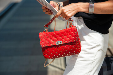 Red leather handbag with iron spikes. Summer urban women's clothing. A woman's hand holds a bag and...