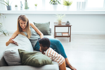 Caucasian woman and young African boy engage with a smartphone, while lounging together on a...