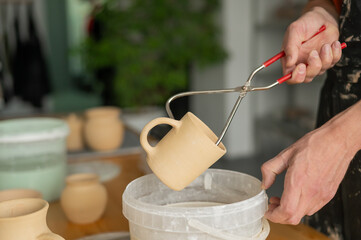 Close-up of a potter's hands glazing a ceramic mug. 