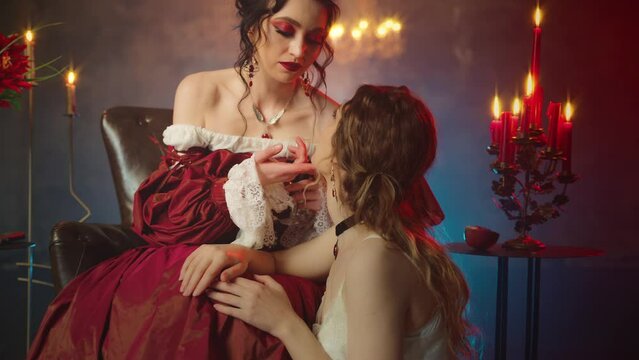 Two women vampires beauty woman black hair Fantasy lady evil queen sitting on throne vampire girl sexy face hypnotizing victim touching with hand maiden gothic old style. dark night room art video 4k