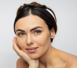 Obraz premium Closeup of beautiful brunette woman with clean perfect skin isolated over white background. Portrait of beauty model touching her face with natural nude makeup. Spa, skincare, wellness.