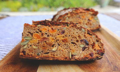 A piece of bread with dried fruits on blue plate, dried apricots, raisins, prunes and hazelnuts, top view.