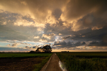 Fototapeta premium Dramatic landscape image of a colorful cloud sky over a country road after the passage of a rain shower