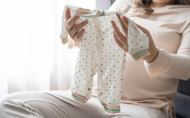 Pregnant asian woman getting ready for the maternity hospital preparing and planning baby clothes for new baby of pregnancy packing for maternity hospital at home