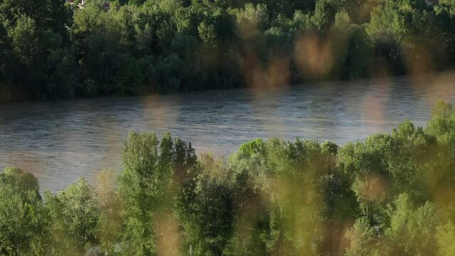 lunga ripresa di una scena tranquilla, con vista in primo piano del fiume isonzo e delle sue sponde verdi, coperte da alti alberi, mentre l'acqua scorre, durante un pomeriggio in estate