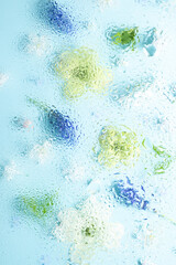 White dogwood flowers blurred behind wet glass. Abstract soft, light floral background. Vertical photo