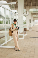 Asian businesswoman with smart phone and coffee waiting for the train at the train station