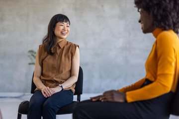 Two businesswomen, one Asian and one African American, converse joyfully in a contemporary office...