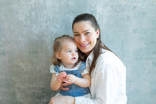 Medium horizontal view of smiling young mother in casual clothes holding blonde toddler daughter looking away with dreamy expression