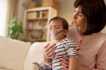 Mother holding baby boy in her arms and giving him an inhalation