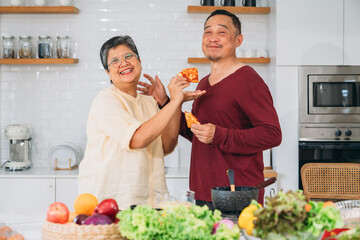 A man and woman are smiling and eating food in a kitchen