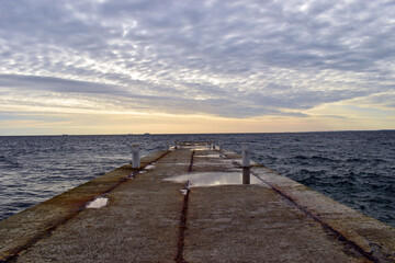 concrete pier, sea view, horizon, sky in clouds. empty concrete pier concept of rest, vacation, summer, trip to the sea, in Odessa. old pier. Image of an outfall with waves and clouds at sunrise