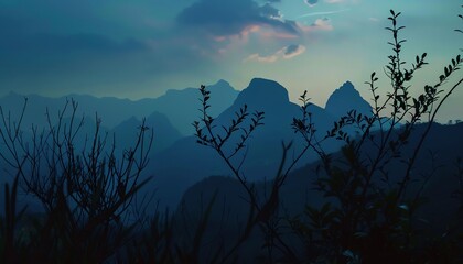 Serene mountain landscape at dusk with silhouetted branches, soft light, and cloudy sky, creating a peaceful and tranquil atmosphere.