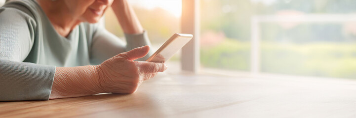 Obraz premium Close-up of elderly woman learning to use a smartphone in the kitchen, focusing on her hand and soft lighting, digital literacy, learning. copy space.