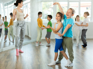Obraz premium Positive preteen children learning to dance waltz in pairs in choreography class
