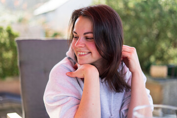 A young beautiful girl in a light hoodie enjoys life while sitting at a table on the terrace of her home. Dolce Vita concept