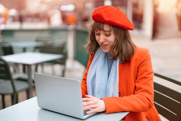 Woman in Red Beret Using Laptop at Outdoor Cafe