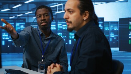 Upbeat african american computer scientist and coworker upgrading equipment in data center. Joyous...