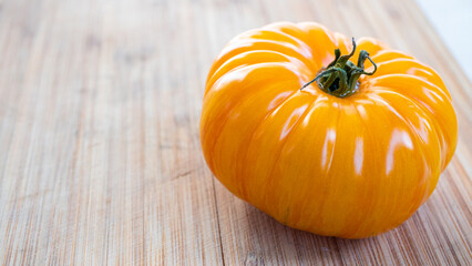 Vibrant and bright orange colored gourmet  tomato sitting on a wooden cutting board. Captured in a highly detailed close up. Green groceries and harvesting season concept.
